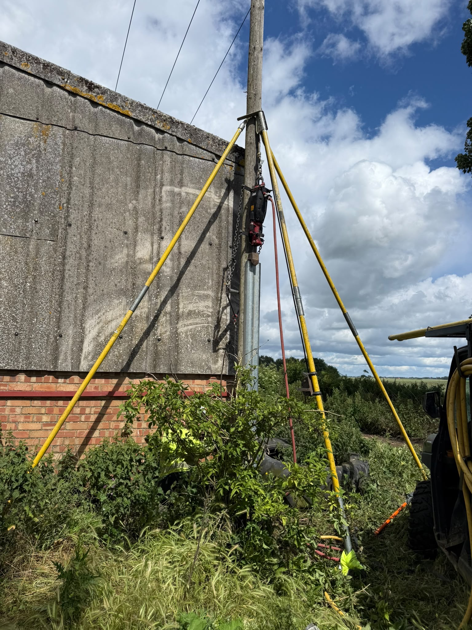 Steel stub extension being fitted to the base of a pole beside a farm building